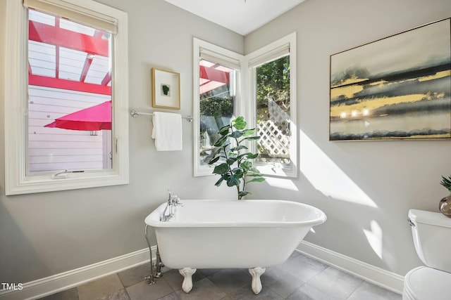 bathroom with a freestanding bath, baseboards, toilet, and tile patterned flooring