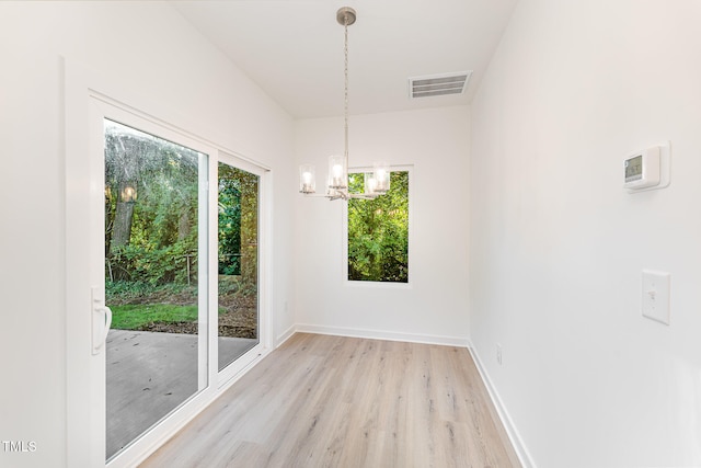 unfurnished dining area featuring an inviting chandelier, light wood finished floors, visible vents, and baseboards