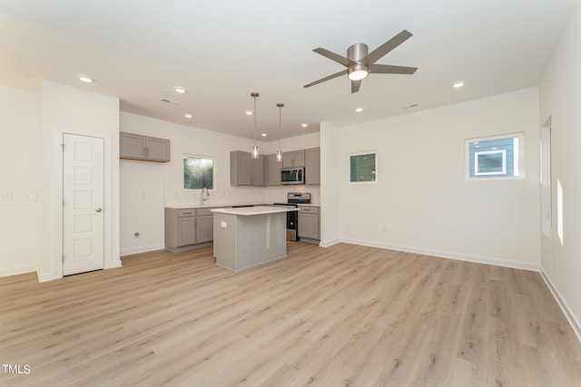 kitchen with gray cabinetry, appliances with stainless steel finishes, decorative light fixtures, and a kitchen island