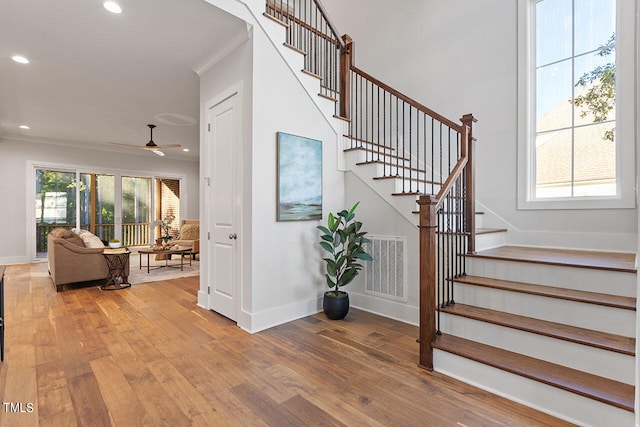 stairs with ornamental molding, hardwood / wood-style floors, and ceiling fan