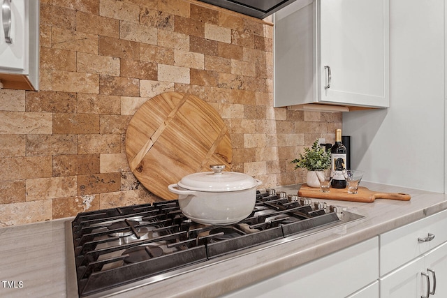 details featuring gas cooktop, tasteful backsplash, light stone countertops, and white cabinets