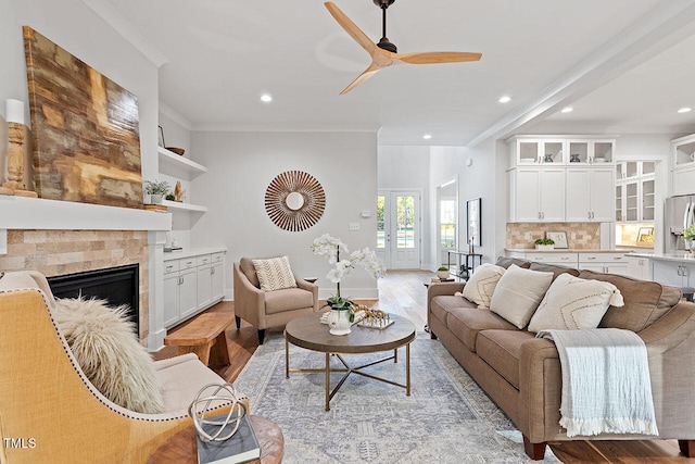 living room featuring ornamental molding, light hardwood / wood-style flooring, a tiled fireplace, and ceiling fan