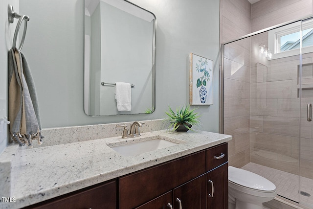 bathroom featuring a shower with door, toilet, and vanity