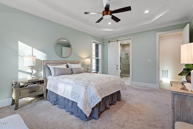 carpeted bedroom with ensuite bathroom, a barn door, a tray ceiling, ceiling fan, and crown molding