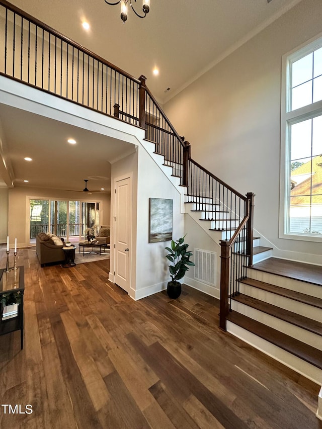 staircase with hardwood / wood-style flooring, ornamental molding, a high ceiling, and an inviting chandelier