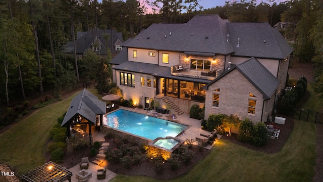 back house at dusk with a gazebo, a pool with hot tub, a lawn, and a patio area