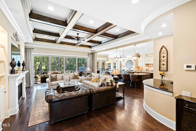 living room featuring beam ceiling, dark wood-type flooring, coffered ceiling, ceiling fan with notable chandelier, and crown molding