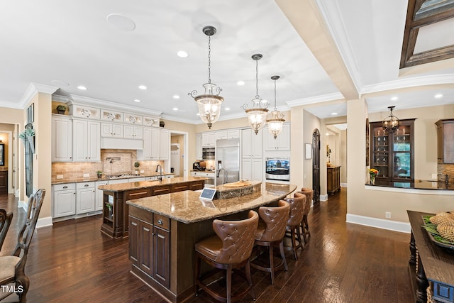 kitchen featuring dark wood-type flooring, a kitchen bar, a kitchen island with sink, and stainless steel appliances