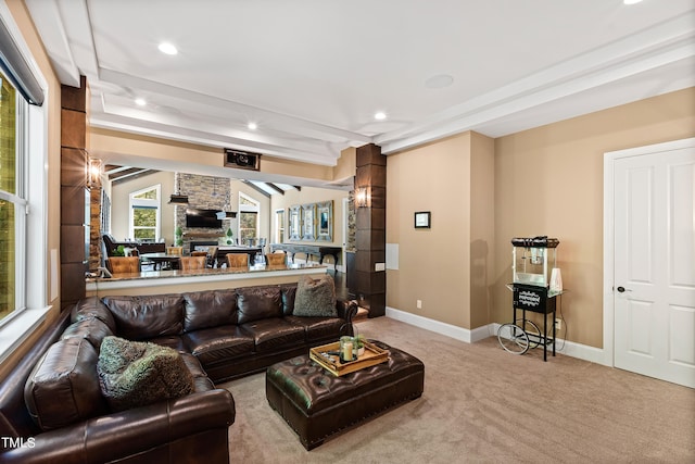 living room with beamed ceiling, a stone fireplace, and light colored carpet