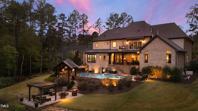 back house at dusk with a patio, an outbuilding, and a lawn