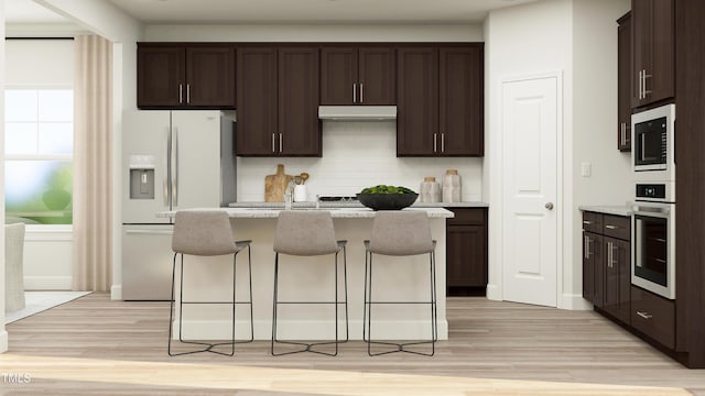 kitchen featuring light stone counters, stainless steel oven, white fridge with ice dispenser, a breakfast bar area, and an island with sink