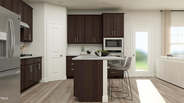 kitchen featuring a center island with sink, a kitchen breakfast bar, sink, stainless steel refrigerator with ice dispenser, and built in microwave