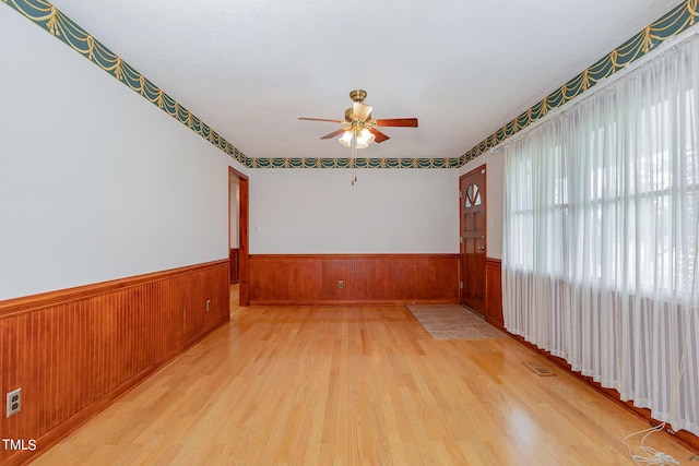 unfurnished room featuring wainscoting, a ceiling fan, wood finished floors, and wooden walls