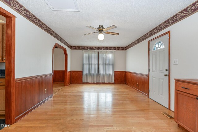 unfurnished room featuring a wainscoted wall, a wealth of natural light, a textured ceiling, and light wood-style flooring