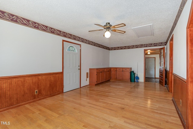 empty room with a ceiling fan, a wainscoted wall, a textured ceiling, and light wood-style floors