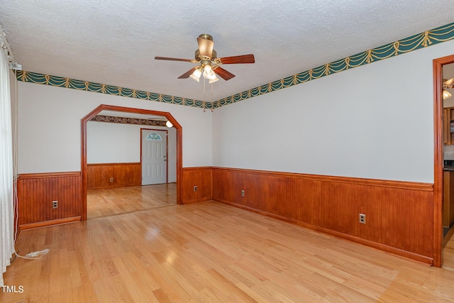 empty room with a textured ceiling, wainscoting, wood finished floors, wood walls, and ceiling fan