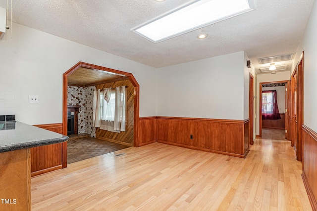 unfurnished living room with light wood finished floors, a wainscoted wall, and a stone fireplace