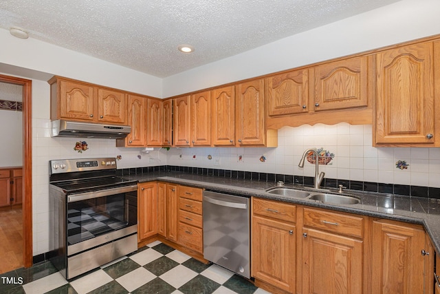 kitchen with dark floors, under cabinet range hood, stainless steel appliances, a sink, and a textured ceiling