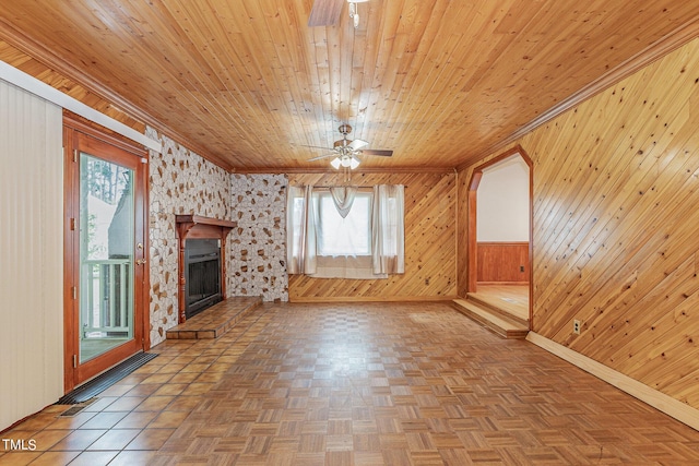 unfurnished living room with ceiling fan, baseboards, ornamental molding, and wood walls