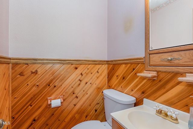 half bath featuring toilet, vanity, and wood walls