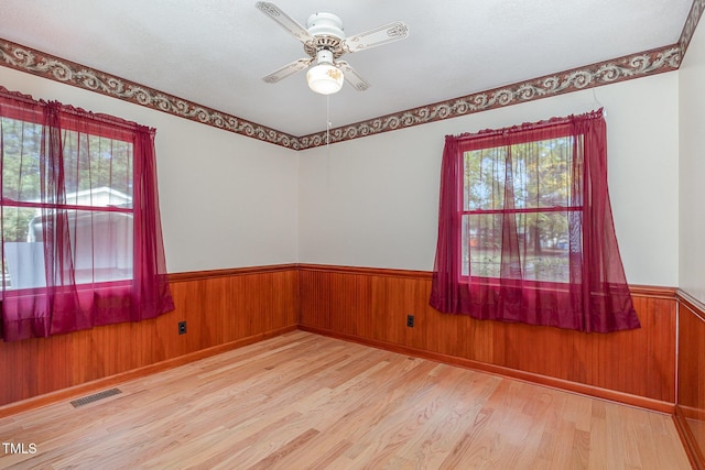 spare room featuring a wainscoted wall, visible vents, wood finished floors, wood walls, and ceiling fan