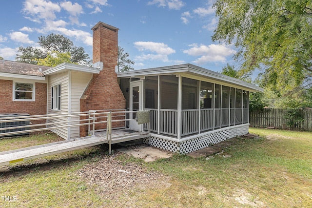 rear view of house with a chimney, fence, a yard, brick siding, and a sunroom