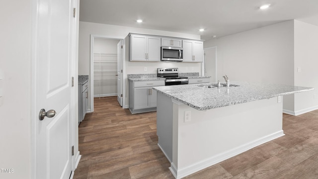 kitchen with stainless steel appliances, wood-type flooring, a center island with sink, and sink