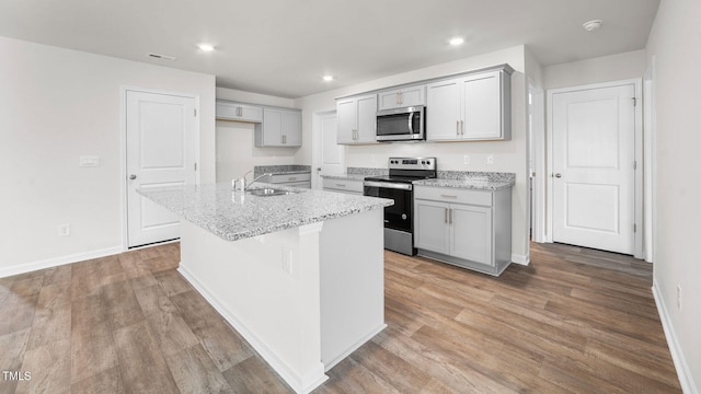 kitchen featuring light stone counters, sink, a kitchen island with sink, appliances with stainless steel finishes, and light wood-type flooring