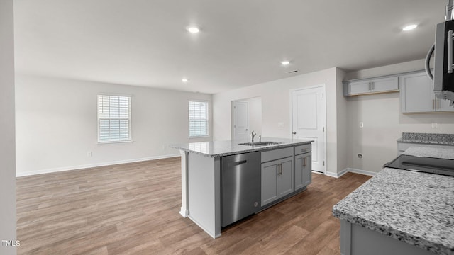 kitchen with light stone countertops, hardwood / wood-style floors, gray cabinetry, appliances with stainless steel finishes, and a center island with sink