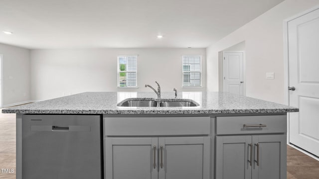 kitchen with sink, gray cabinetry, stainless steel dishwasher, a center island with sink, and light stone countertops