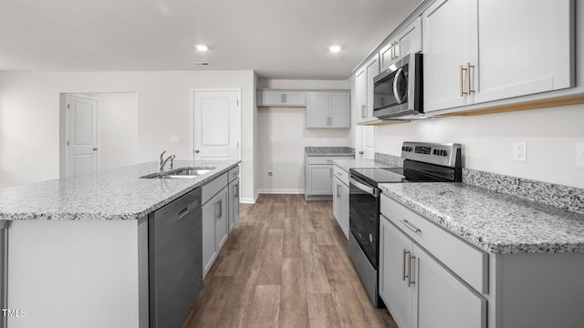 kitchen featuring a kitchen island with sink, light wood-type flooring, sink, light stone countertops, and appliances with stainless steel finishes