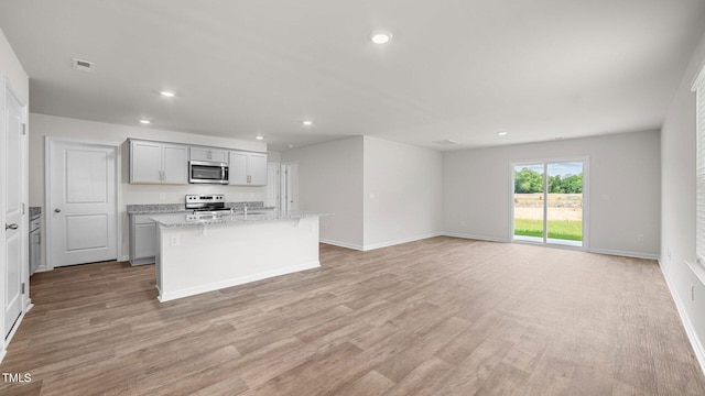 kitchen with an island with sink, light wood-type flooring, light stone counters, stainless steel appliances, and a breakfast bar area