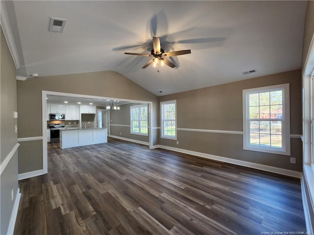 unfurnished living room featuring ceiling fan with notable chandelier, a healthy amount of sunlight, dark wood-type flooring, and vaulted ceiling