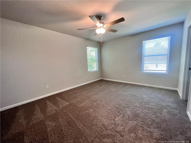 unfurnished room featuring dark colored carpet, ceiling fan, and a wealth of natural light