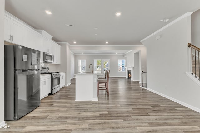 kitchen with appliances with stainless steel finishes, light hardwood / wood-style flooring, an island with sink, and white cabinets