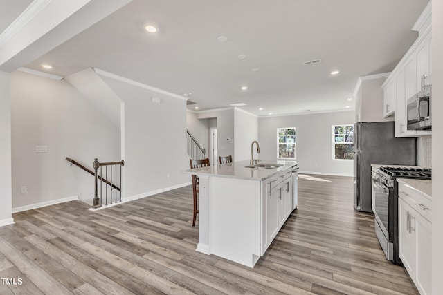 kitchen with an island with sink, light hardwood / wood-style flooring, stainless steel appliances, and white cabinetry