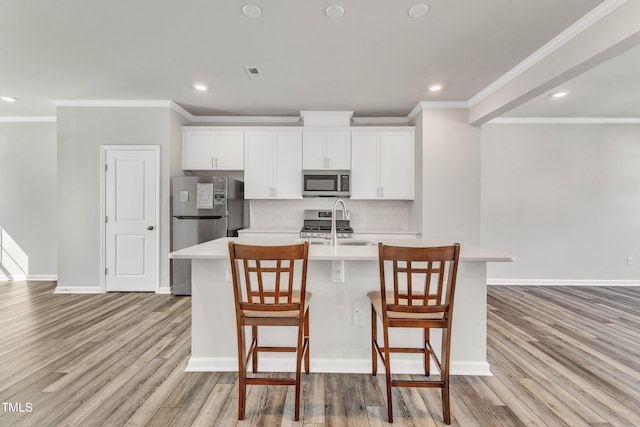 kitchen featuring a kitchen island with sink, a breakfast bar area, light hardwood / wood-style flooring, stainless steel appliances, and white cabinetry