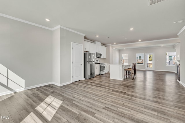 kitchen with an island with sink, appliances with stainless steel finishes, a kitchen breakfast bar, white cabinetry, and light hardwood / wood-style flooring