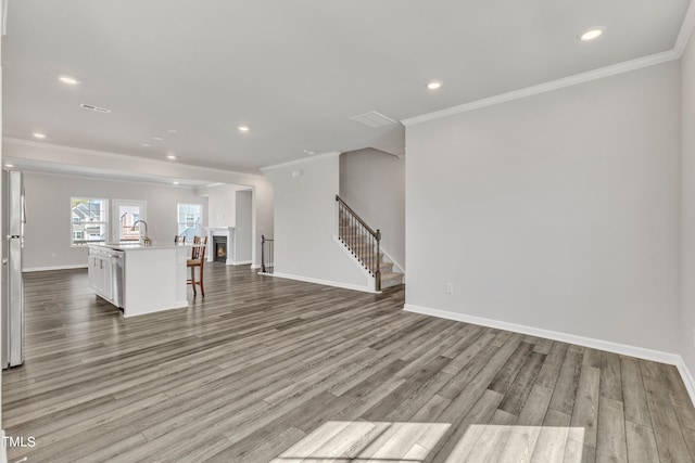 unfurnished living room with sink, crown molding, and light hardwood / wood-style floors