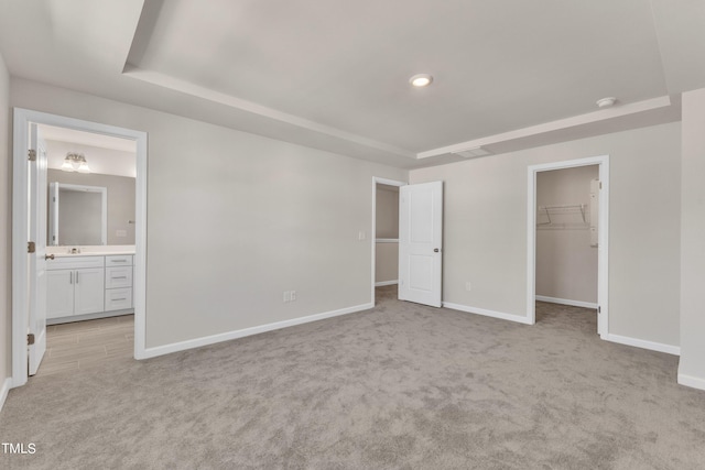 unfurnished bedroom featuring a closet, light carpet, a tray ceiling, a spacious closet, and ensuite bathroom