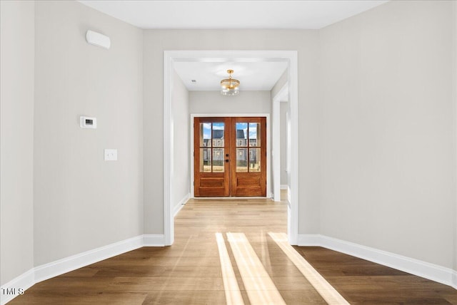 doorway to outside featuring french doors, light wood-type flooring, and an inviting chandelier