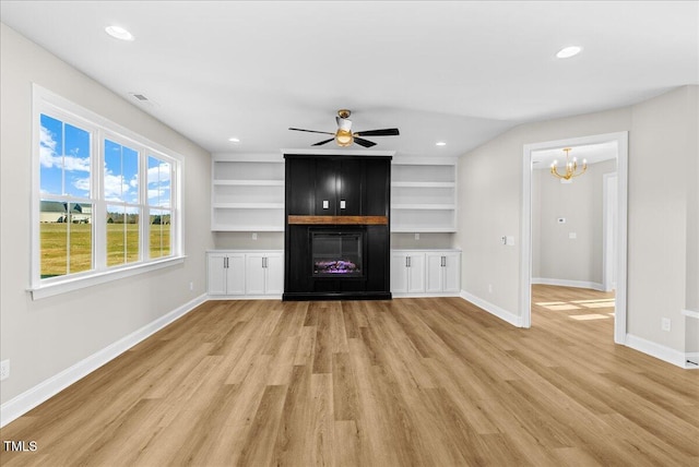 unfurnished living room with built in shelves, a large fireplace, ceiling fan with notable chandelier, and light hardwood / wood-style flooring