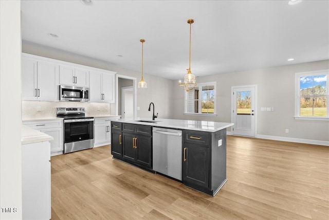 kitchen featuring white cabinets, sink, appliances with stainless steel finishes, decorative light fixtures, and light hardwood / wood-style floors