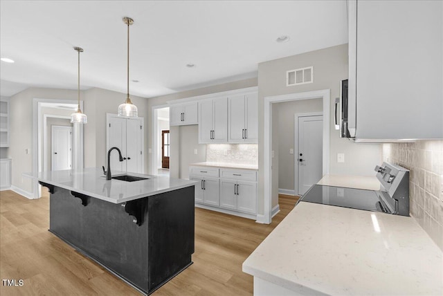 kitchen with stove, sink, decorative backsplash, decorative light fixtures, and white cabinetry