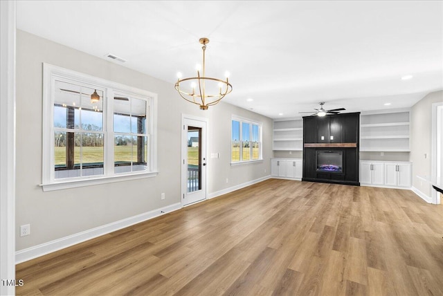 unfurnished living room with light hardwood / wood-style floors, ceiling fan with notable chandelier, a large fireplace, and built in features