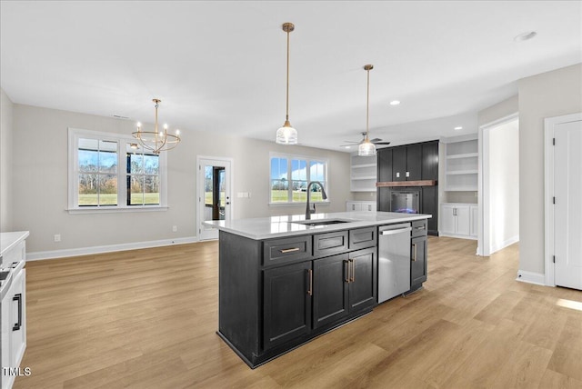 kitchen with dishwasher, a kitchen island with sink, ceiling fan with notable chandelier, sink, and built in shelves