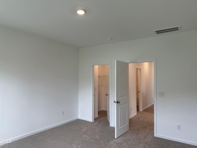 unfurnished bedroom featuring a walk in closet, carpet floors, baseboards, visible vents, and a closet
