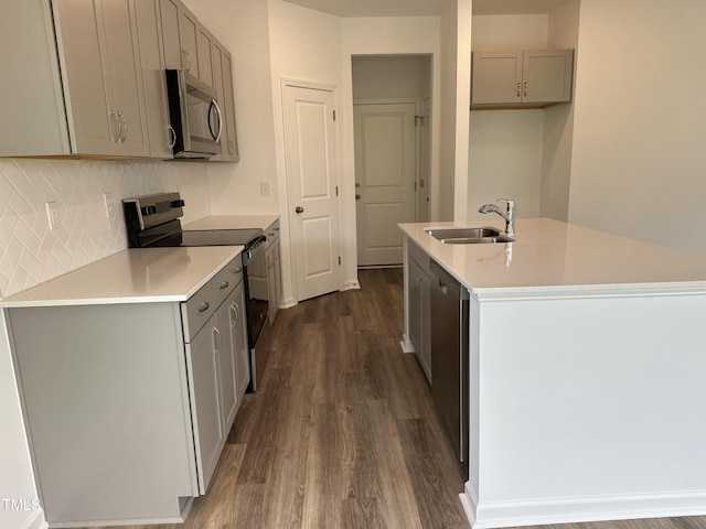 kitchen featuring appliances with stainless steel finishes, a sink, an island with sink, gray cabinets, and dark wood-type flooring