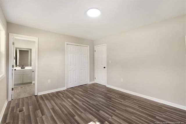 unfurnished bedroom featuring a closet, dark hardwood / wood-style floors, sink, and ensuite bath