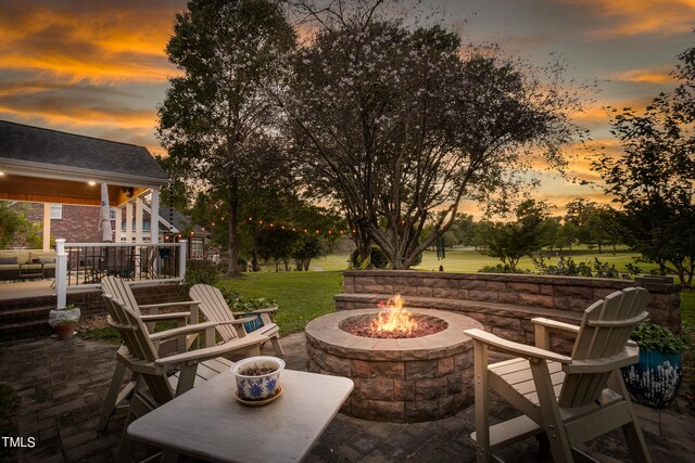 patio terrace at dusk with a yard, a deck, and a fire pit